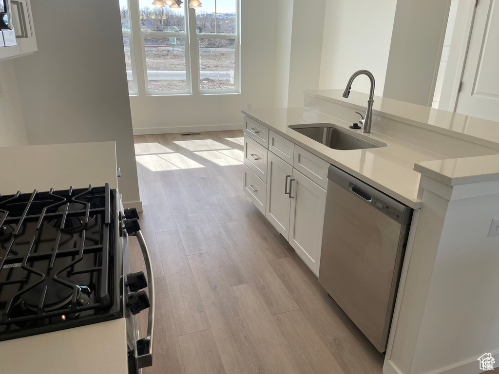 Kitchen with stainless steel dishwasher, light wood-style flooring, a sink, white cabinetry, and gas stove