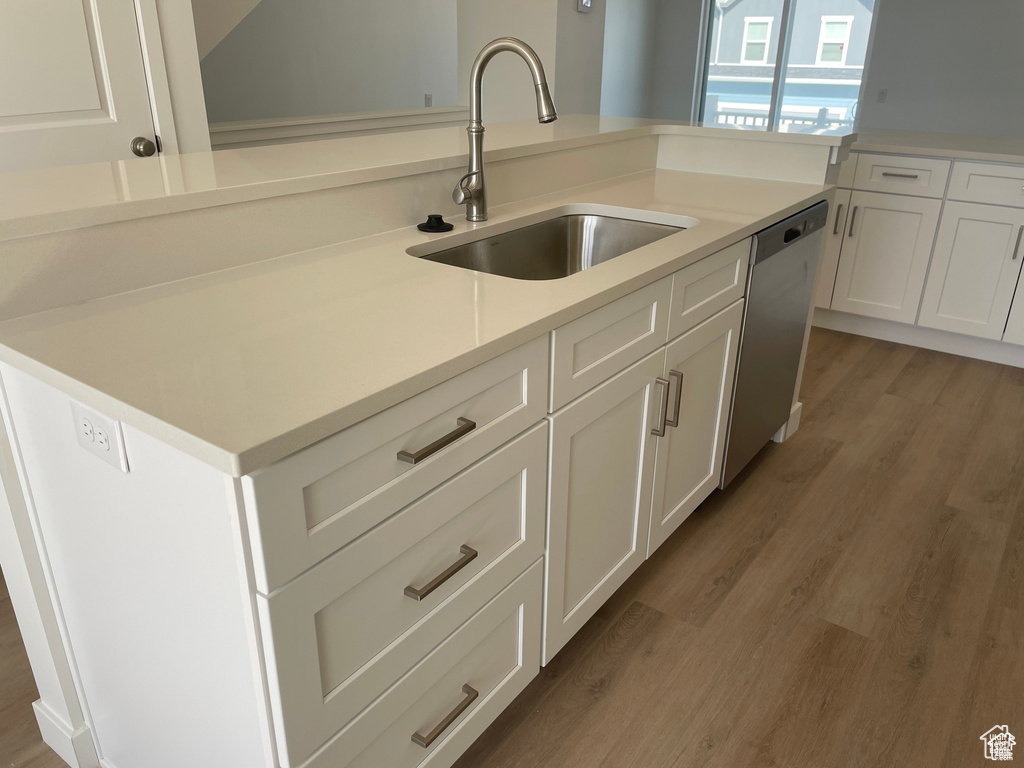 Kitchen featuring white cabinets, light wood-style floors, dishwasher, and a sink