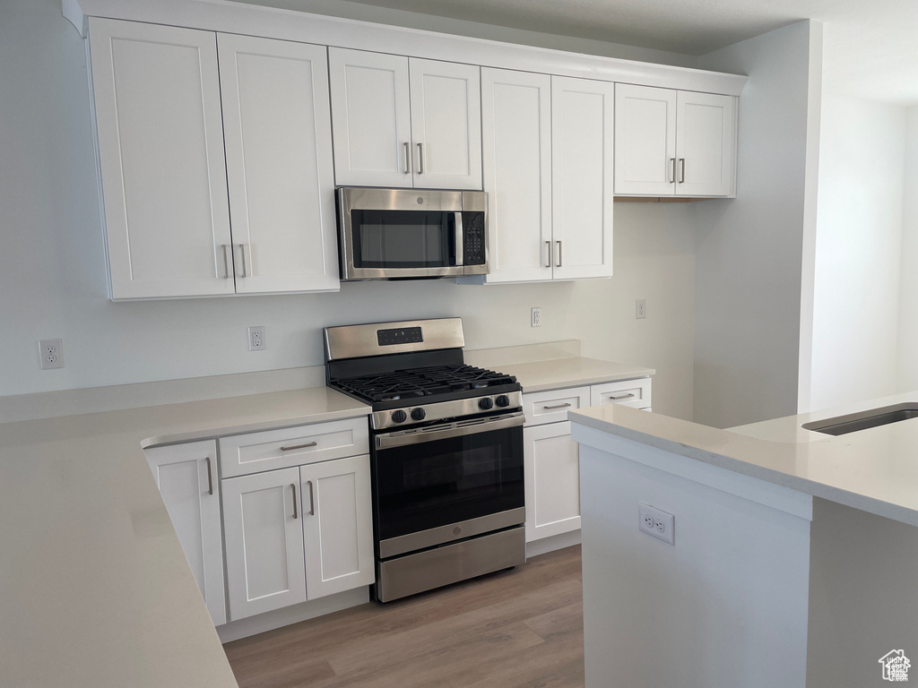 Kitchen with white cabinets, appliances with stainless steel finishes, light wood-style floors, and light countertops