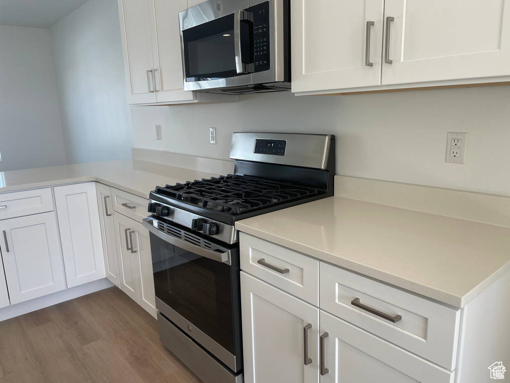 Kitchen with white cabinets, light countertops, wood finished floors, and appliances with stainless steel finishes