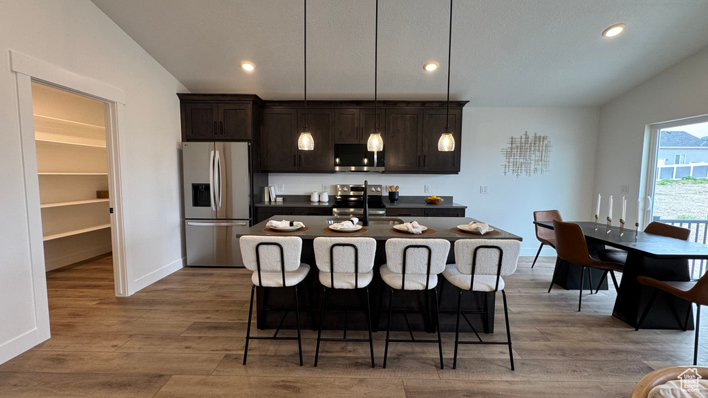 Kitchen with a kitchen breakfast bar, dark countertops, vaulted ceiling, a center island with sink, and stainless steel appliances