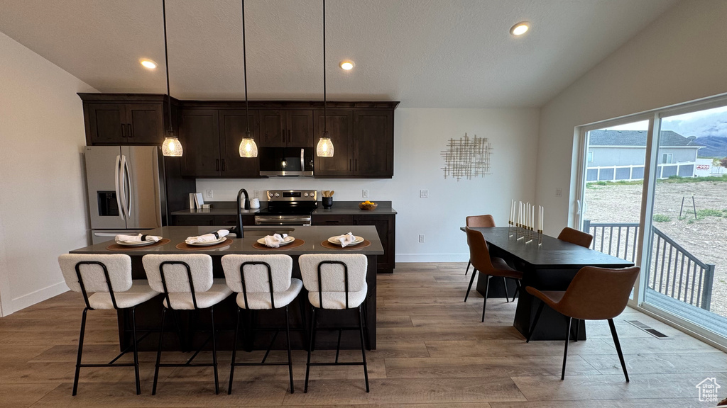 Kitchen with wood finished floors, appliances with stainless steel finishes, lofted ceiling, and dark countertops
