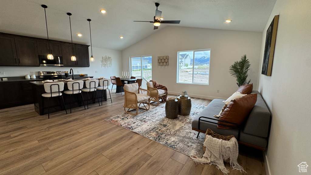 Living room with ceiling fan, vaulted ceiling, baseboards, light wood finished floors, and recessed lighting