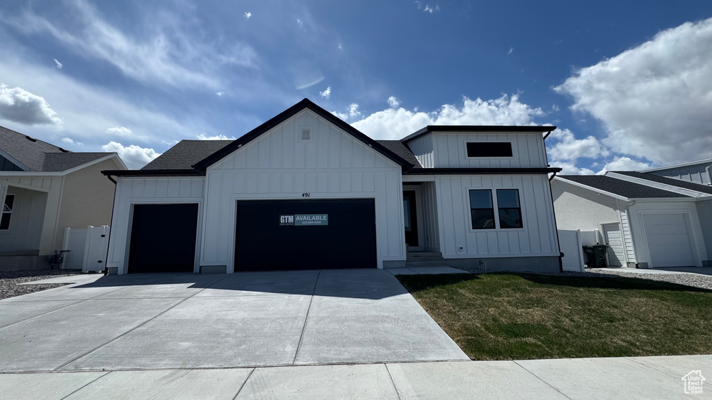 Modern farmhouse style home with concrete driveway, a front lawn, board and batten siding, and a garage