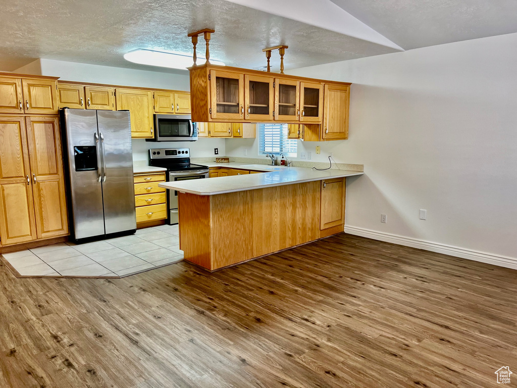 Kitchen with appliances with stainless steel finishes, light wood-style floors, a peninsula, light countertops, and glass insert cabinets