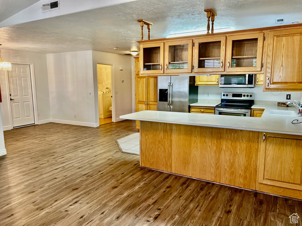 Kitchen with appliances with stainless steel finishes, light countertops, a peninsula, wood finished floors, and glass insert cabinets