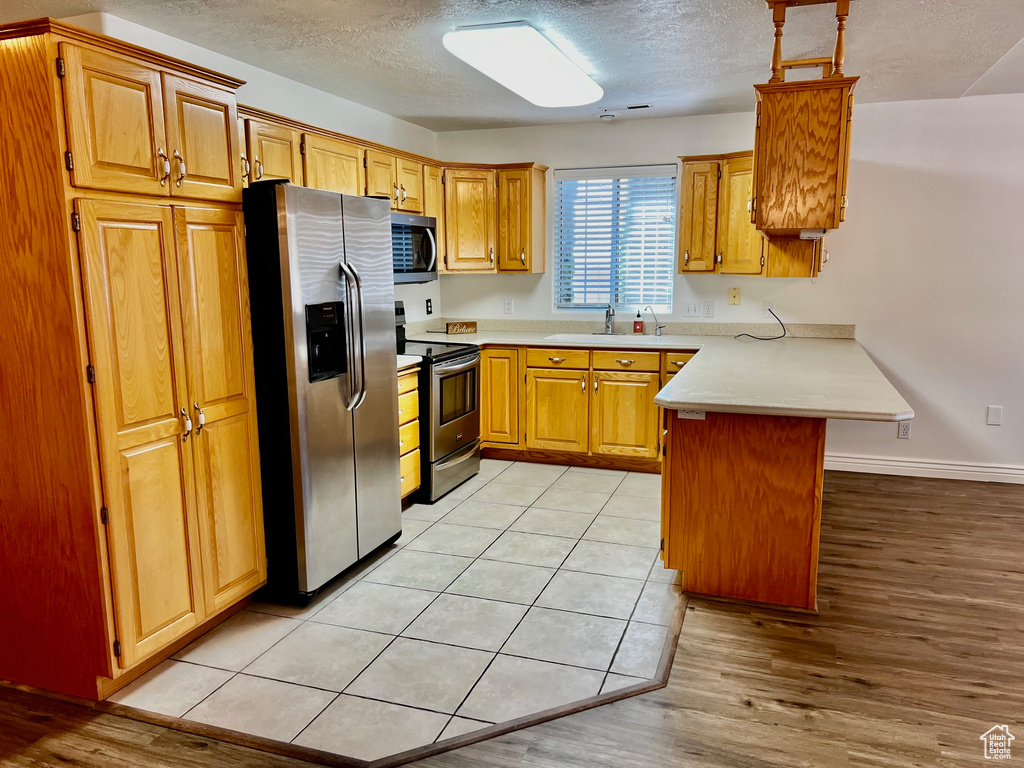 Kitchen with stainless steel appliances, a peninsula, light countertops, light wood-type flooring, and a textured ceiling