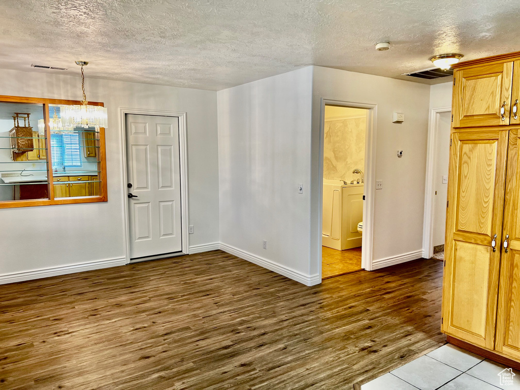Empty room with a textured ceiling, wood finished floors, a smoke detector, and a chandelier