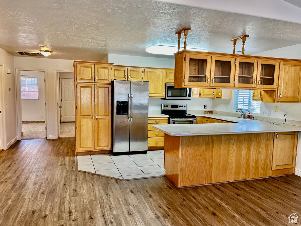 Kitchen featuring appliances with stainless steel finishes, a peninsula, light wood-style floors, light countertops, and glass insert cabinets