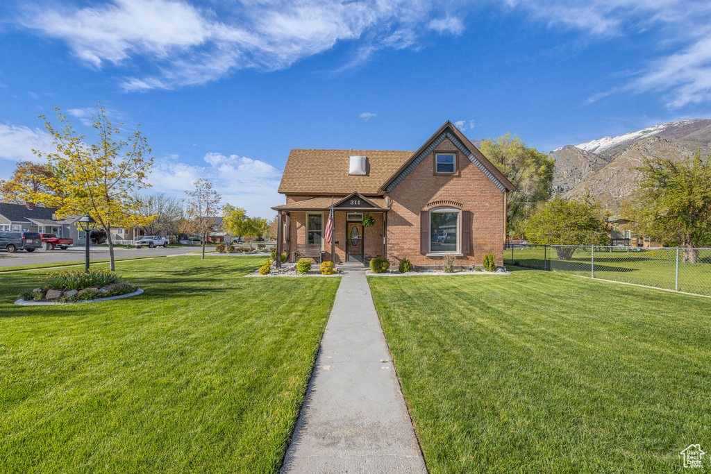 View of front facade with brick siding, a front lawn, fence, and a mountain view