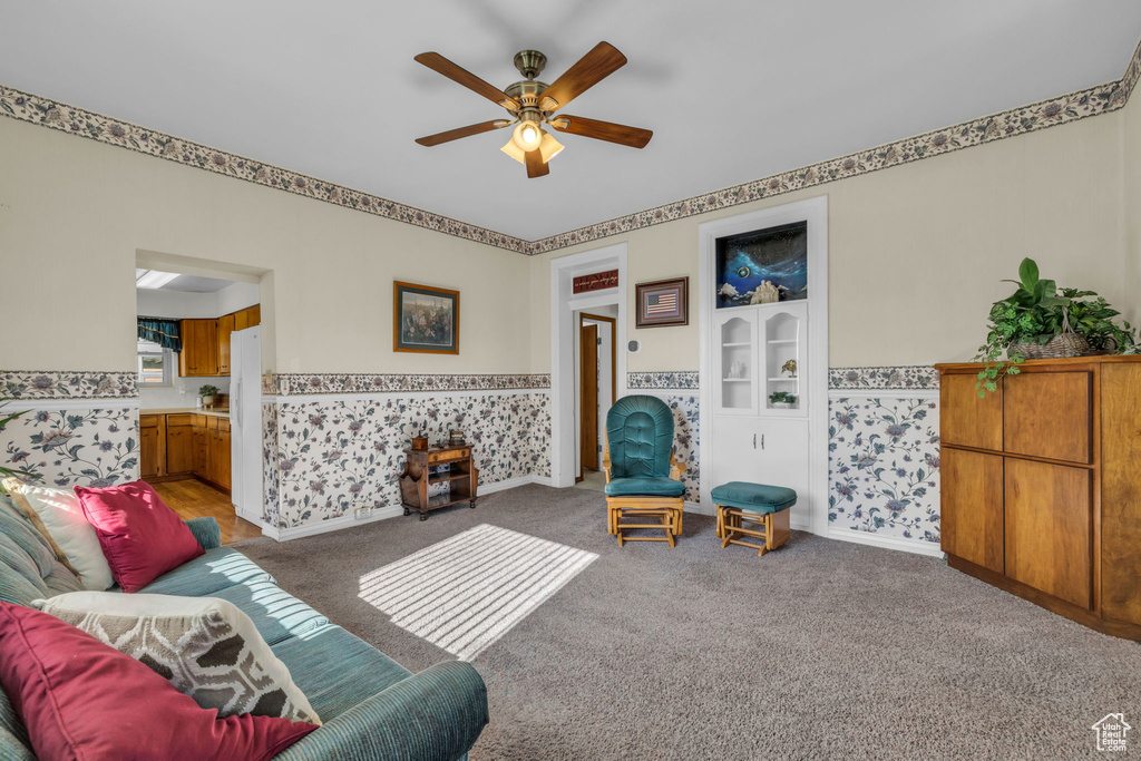 Living area with wallpapered walls, a wainscoted wall, carpet, and ceiling fan
