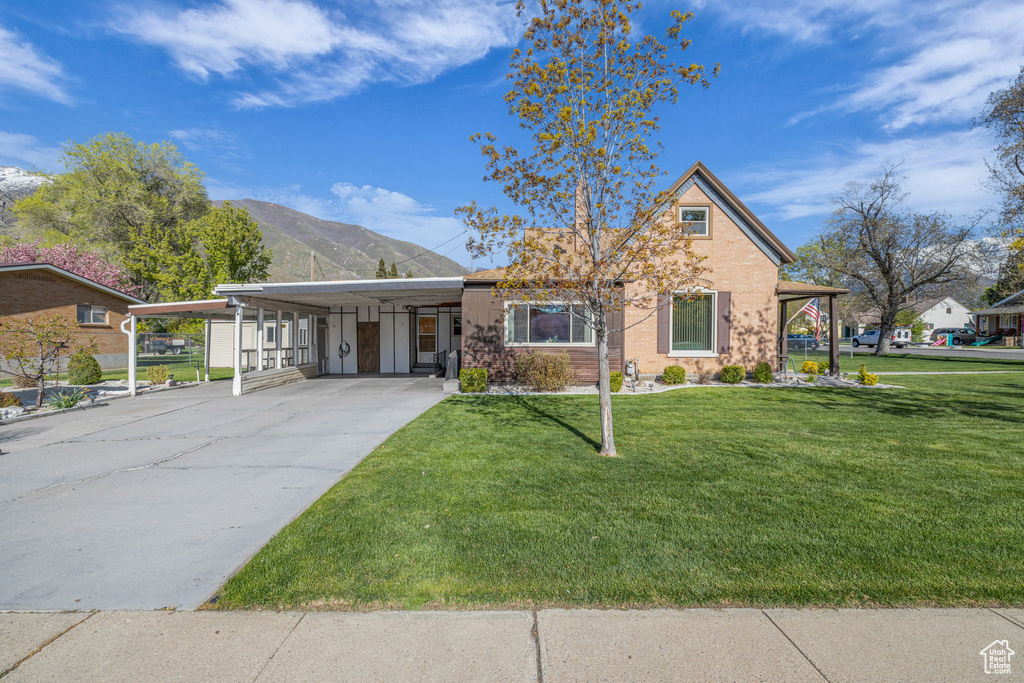 View of front of house with driveway, a mountain view, a front yard, and an attached carport