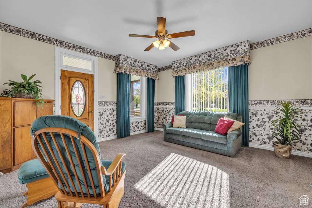 Carpeted living room with wainscoting, a ceiling fan, and wallpapered walls