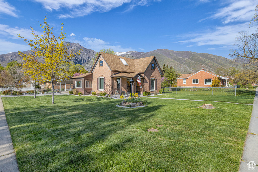 View of front of house with fence, a front lawn, roof with shingles, brick siding, and a mountain view