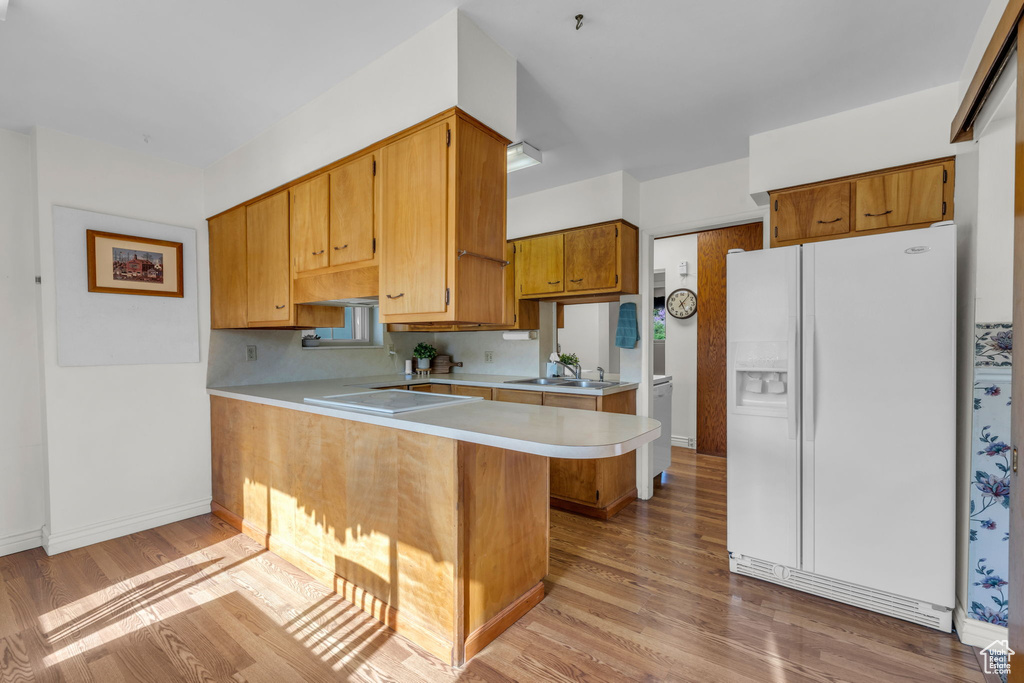 Kitchen featuring a sink, white fridge with ice dispenser, light wood-type flooring, light countertops, and a peninsula