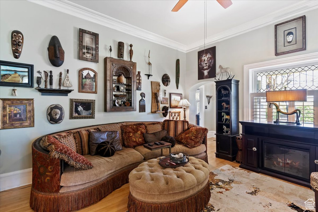 Living area featuring arched walkways, a glass covered fireplace, a ceiling fan, wood finished floors, and ornamental molding