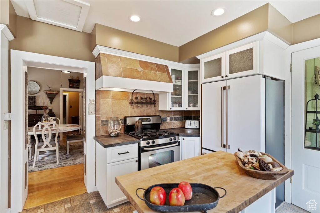 Kitchen featuring backsplash, high end white refrigerator, premium range hood, gas stove, and white cabinetry