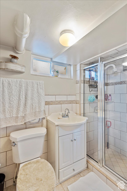 Full bath with tile patterned floors, toilet, vanity, tile walls, and a stall shower