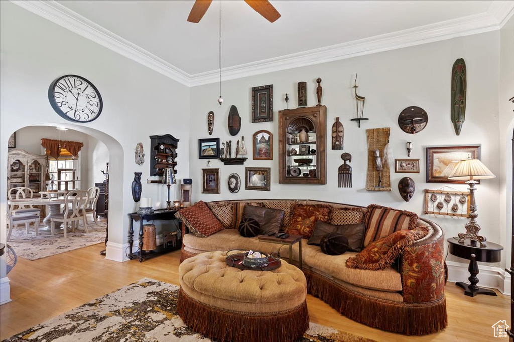 Living area featuring ceiling fan, arched walkways, crown molding, and light wood finished floors