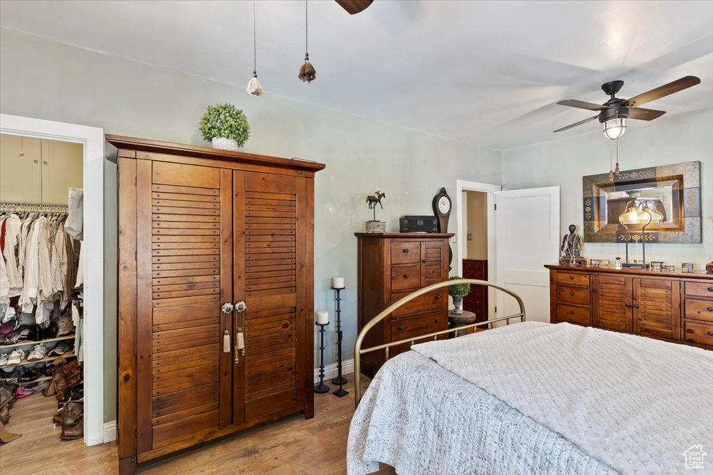 Bedroom featuring wood finished floors, a spacious closet, a ceiling fan, and baseboards