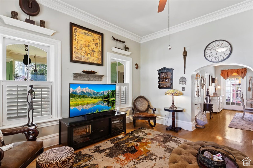 Living room with arched walkways, ornamental molding, wood finished floors, and a healthy amount of sunlight