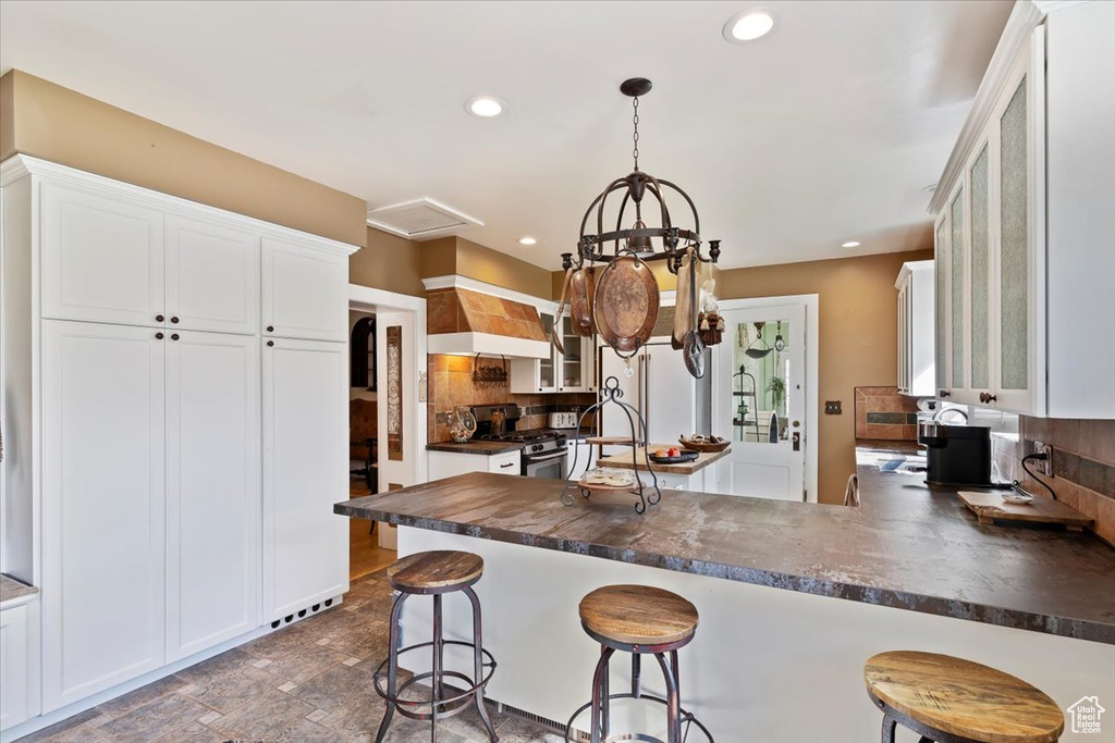 Kitchen with dark countertops, glass insert cabinets, custom range hood, and stainless steel gas range