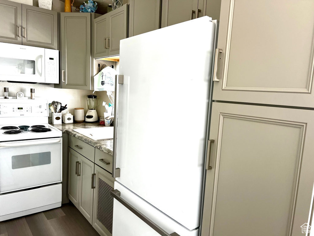 Kitchen with gray cabinetry, white appliances, and dark wood-type flooring