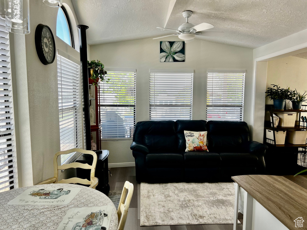Living room with vaulted ceiling, wood finished floors, a textured ceiling, and a ceiling fan