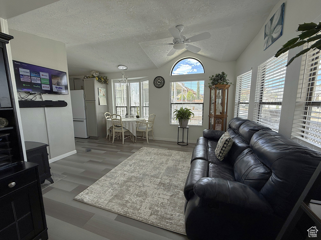 Living room featuring vaulted ceiling, a textured ceiling, ceiling fan, baseboards, and wood finished floors