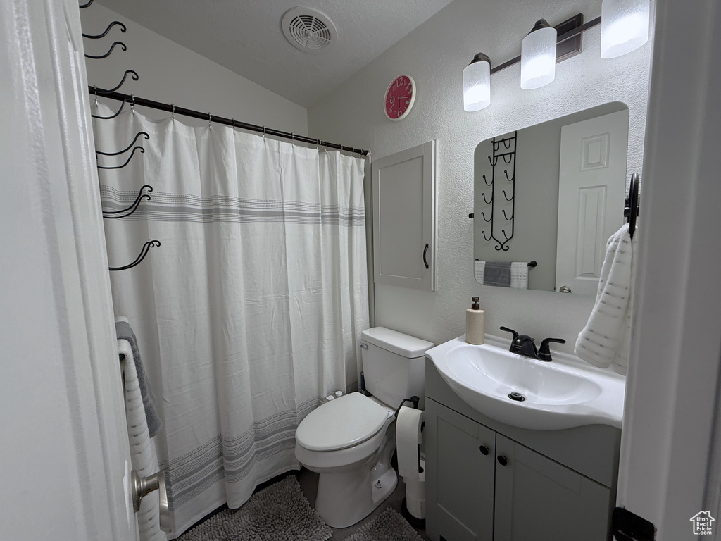 Full bath with toilet, lofted ceiling, vanity, a textured wall, and a shower with curtain