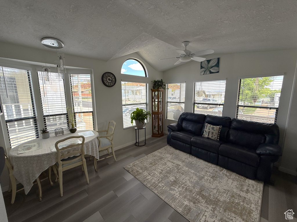 Living area featuring ceiling fan, a textured ceiling, light wood finished floors, vaulted ceiling, and baseboards