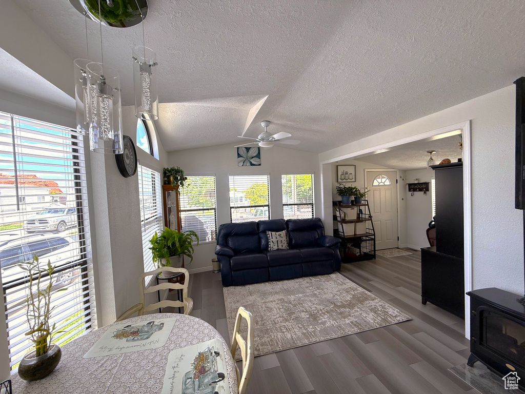 Living area featuring a textured ceiling, a ceiling fan, wood finished floors, lofted ceiling, and a wood stove