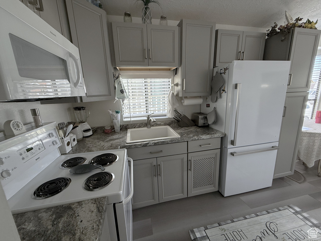 Kitchen featuring white appliances, gray cabinetry, a sink, and a textured ceiling