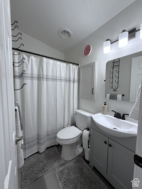 Full bath featuring a textured ceiling, vanity, a textured wall, toilet, and curtained shower