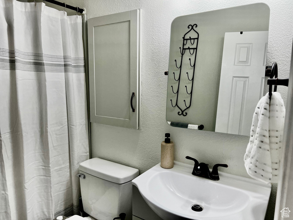 Bathroom featuring a textured wall, toilet, vanity, and a shower with curtain
