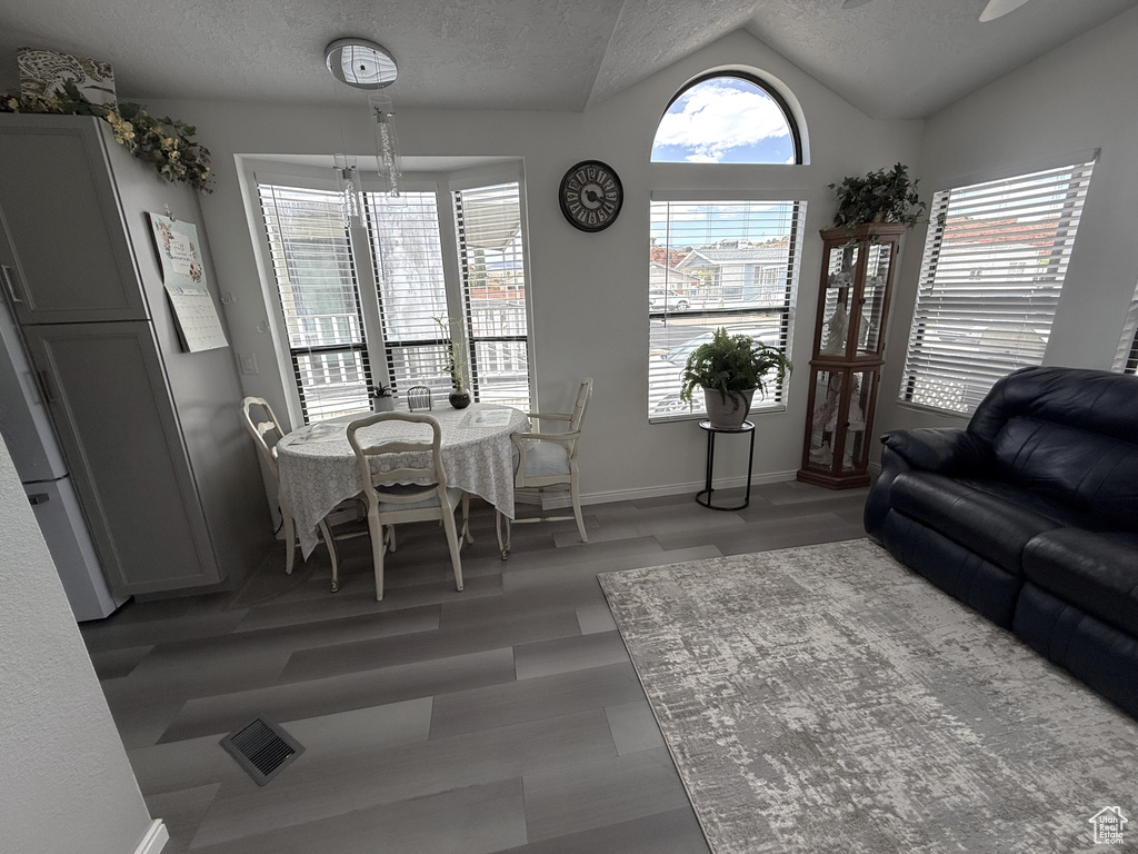 Living room with light wood finished floors, vaulted ceiling, baseboards, and a textured ceiling