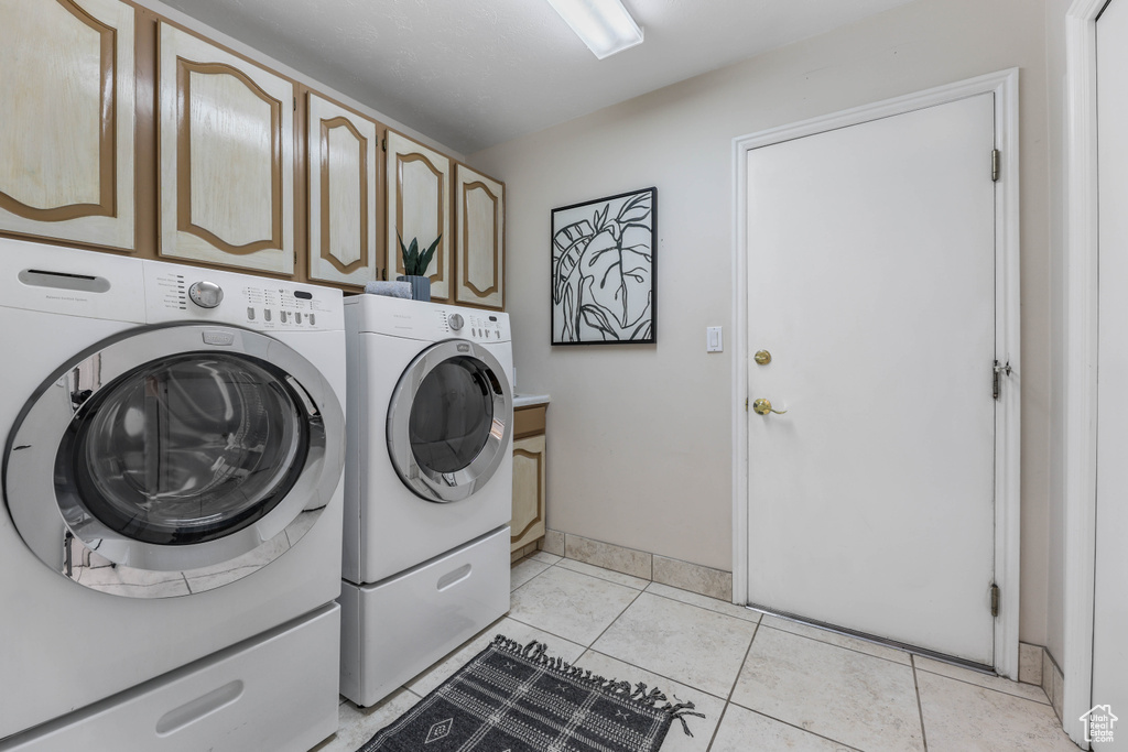 Laundry area featuring washing machine and dryer, baseboards, cabinet space, and light tile patterned floors