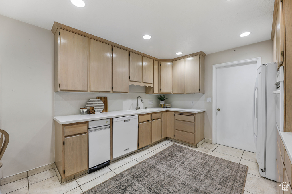 Kitchen with light brown cabinetry, a sink, white appliances, and light countertops