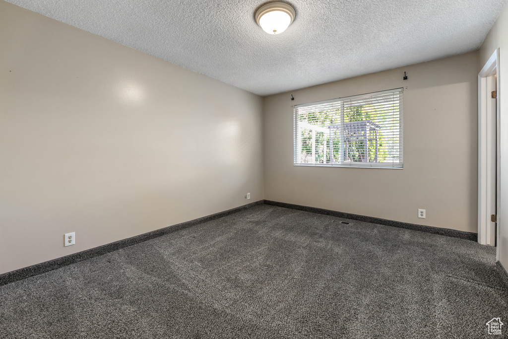Spare room featuring dark colored carpet, baseboards, and a textured ceiling