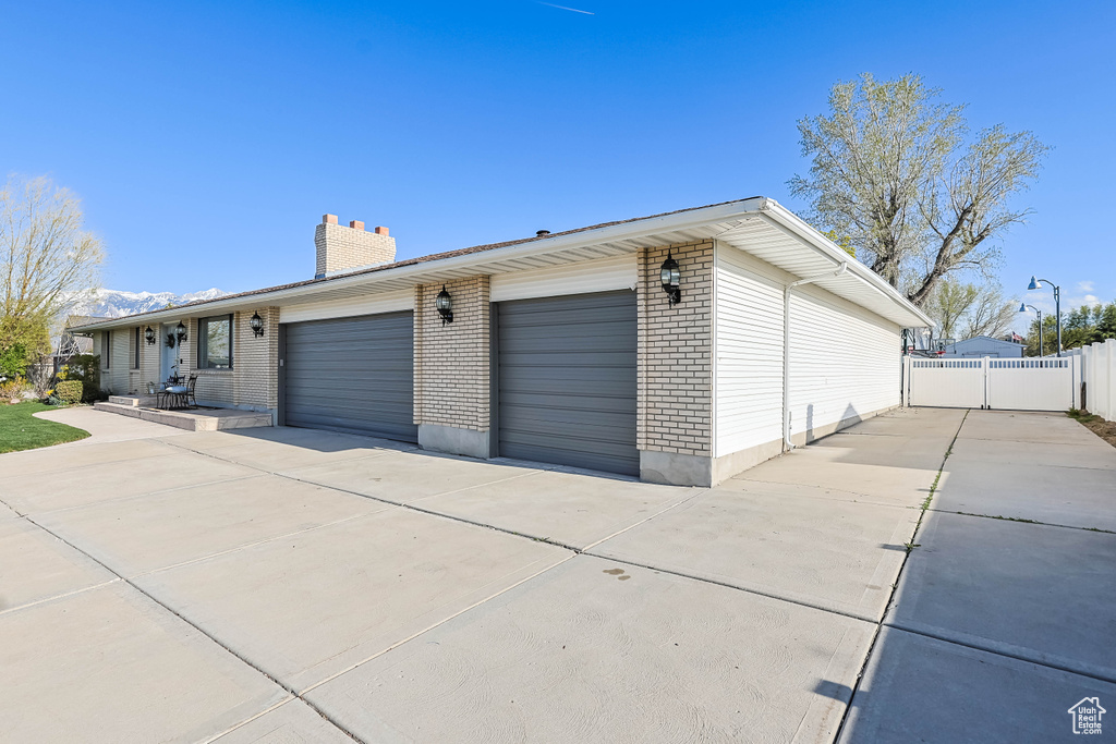 Exterior space featuring a chimney, fence, concrete driveway, an attached garage, and brick siding