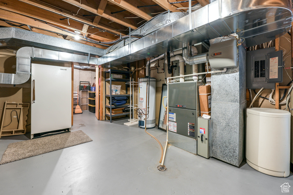 Unfinished basement featuring freestanding refrigerator, gas water heater, and electric panel