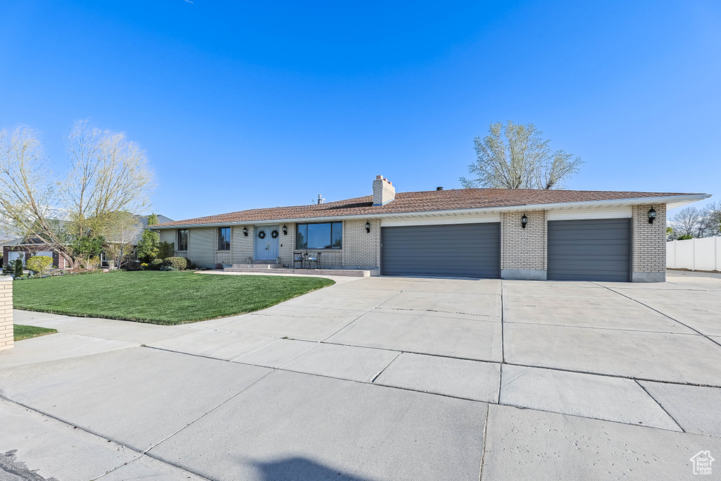 Ranch-style house featuring a chimney, concrete driveway, brick siding, a front yard, and a garage