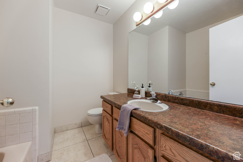 Bathroom with a tub to relax in, tile patterned floors, visible vents, toilet, and vanity