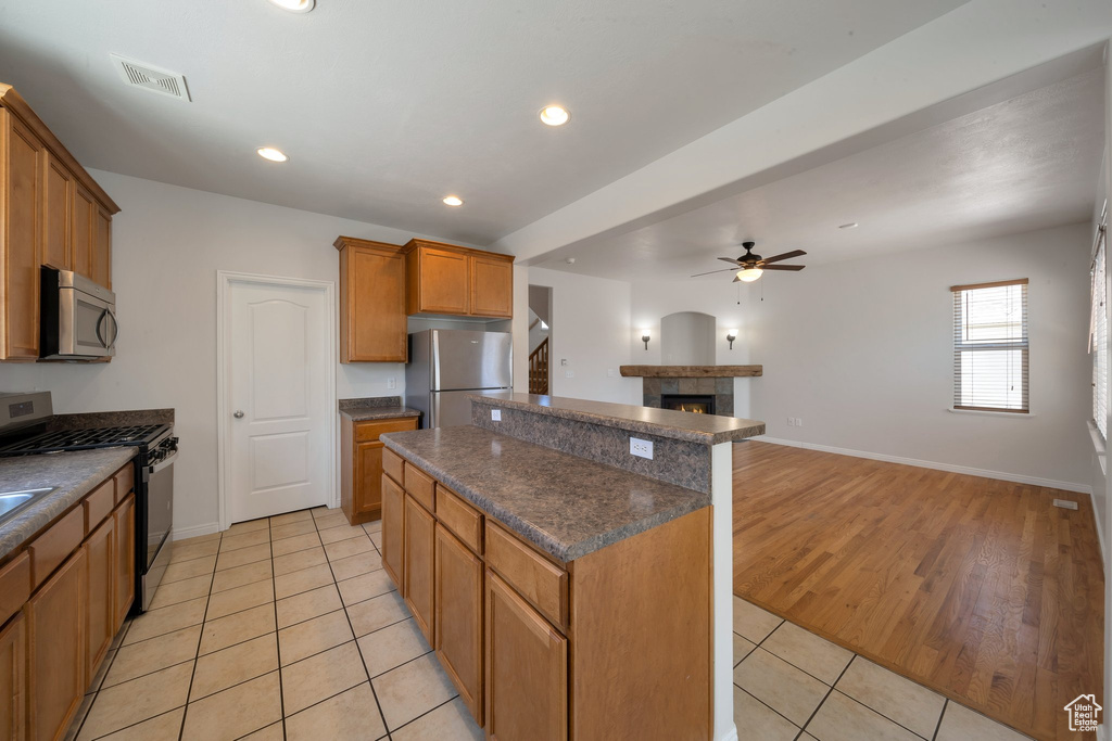 Kitchen with stainless steel appliances, dark countertops, a ceiling fan, light tile patterned floors, and a kitchen island