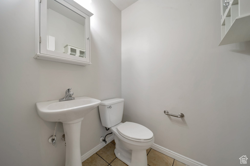 Half bathroom featuring baseboards, toilet, tile patterned flooring, and a sink