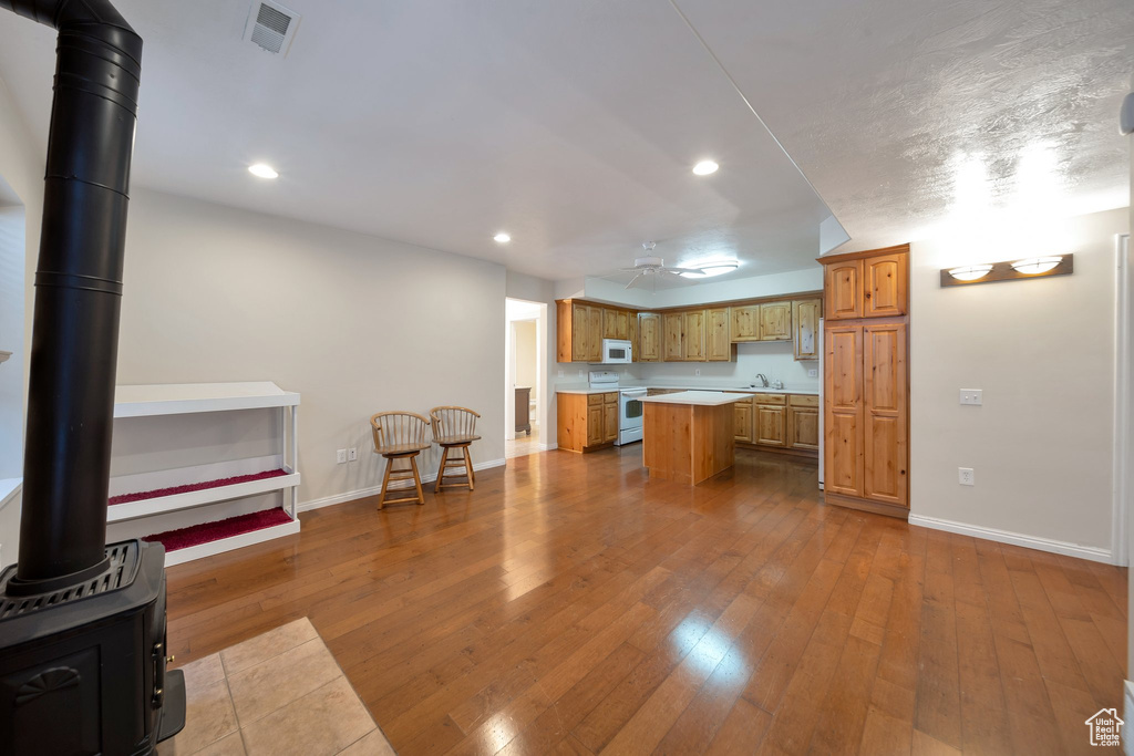 Kitchen featuring baseboards, white appliances, light countertops, a kitchen island, and a wood stove