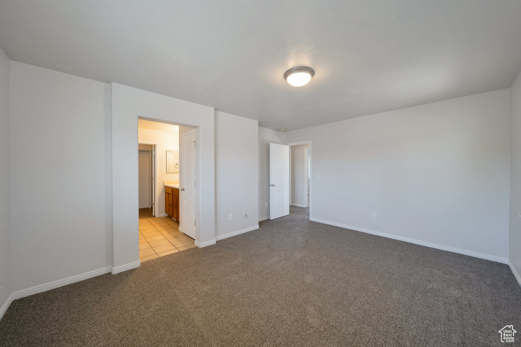 Unfurnished bedroom featuring light colored carpet, baseboards, connected bathroom, and light tile patterned floors