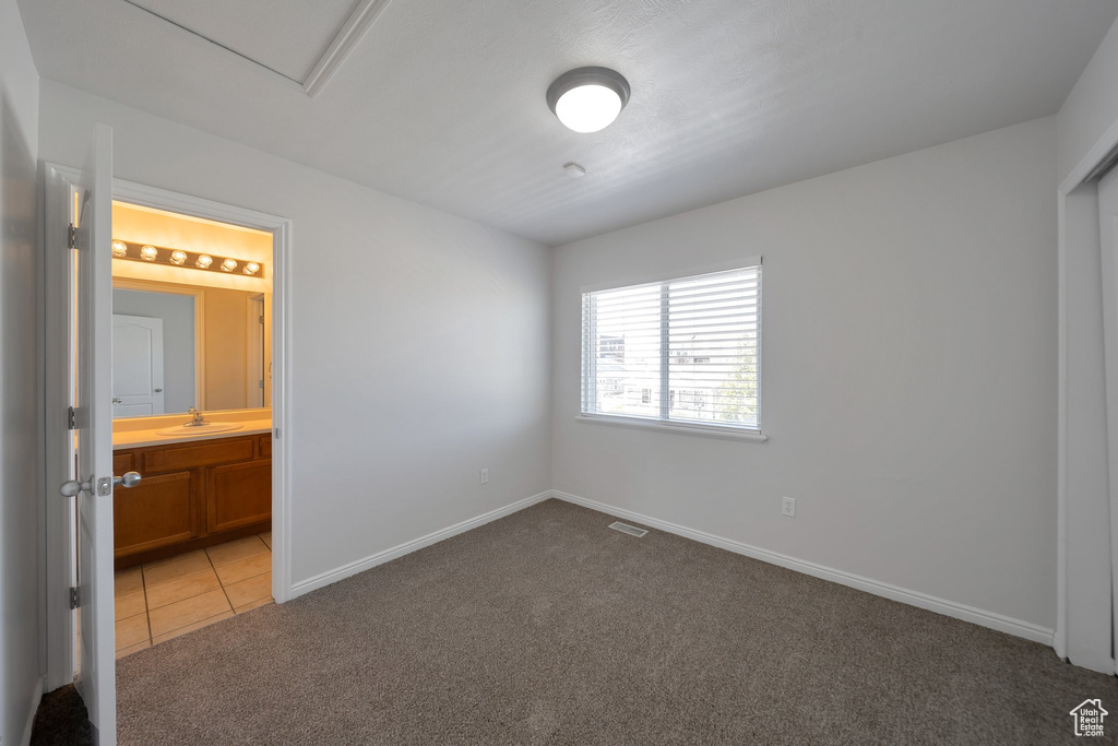 Unfurnished bedroom featuring visible vents, light carpet, a sink, ensuite bath, and baseboards