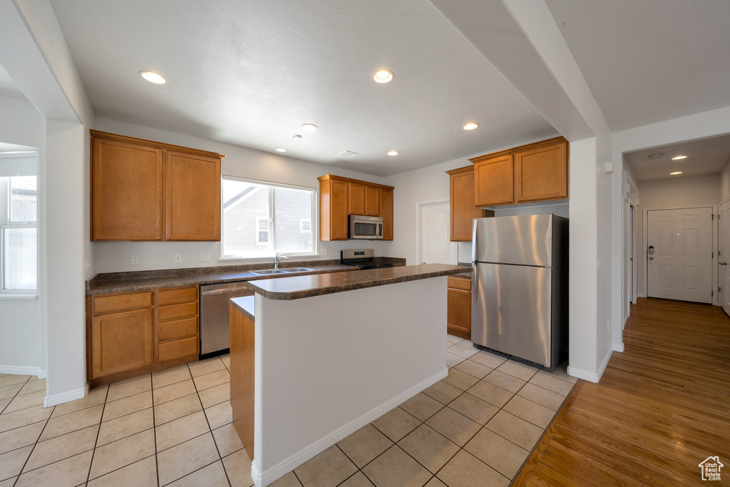 Kitchen featuring stainless steel appliances, a sink, baseboards, brown cabinets, and a kitchen island