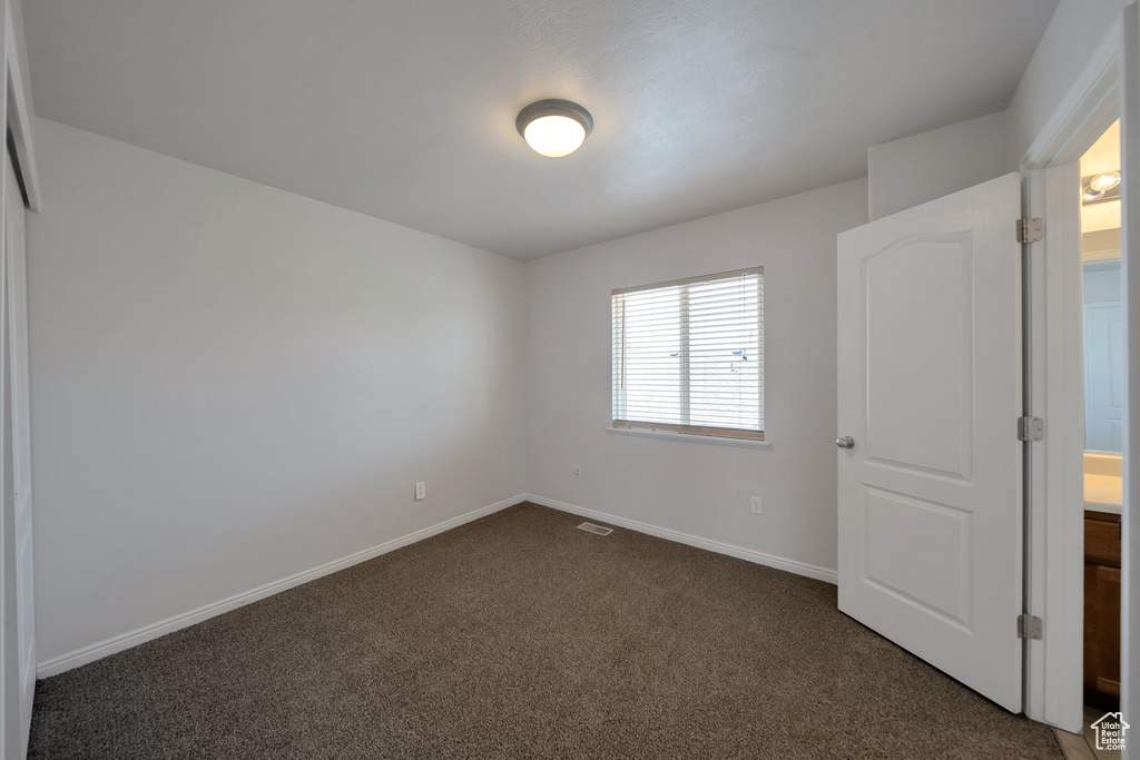 Unfurnished bedroom with visible vents, dark colored carpet, and baseboards